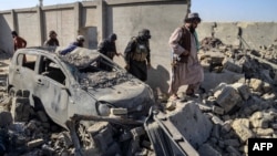 Taliban security personnel walk past a damaged car in the Spin Boldak district of Kandahar province on October 16, 2025, a day after the cross-border clashes between Afghanistan and Pakistan.